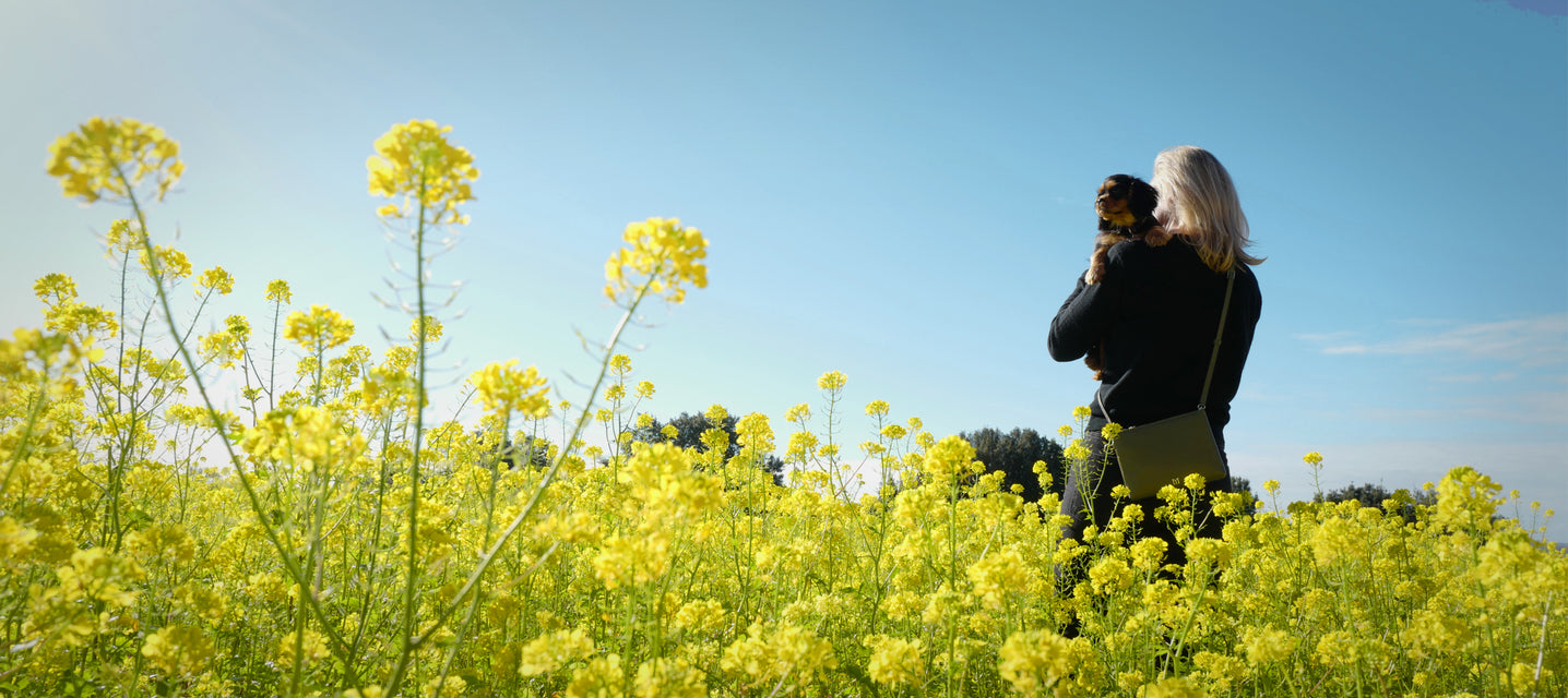 woman holding a dog and Maison Marrain DeuxVie small pouch in vine green in yellow flower field