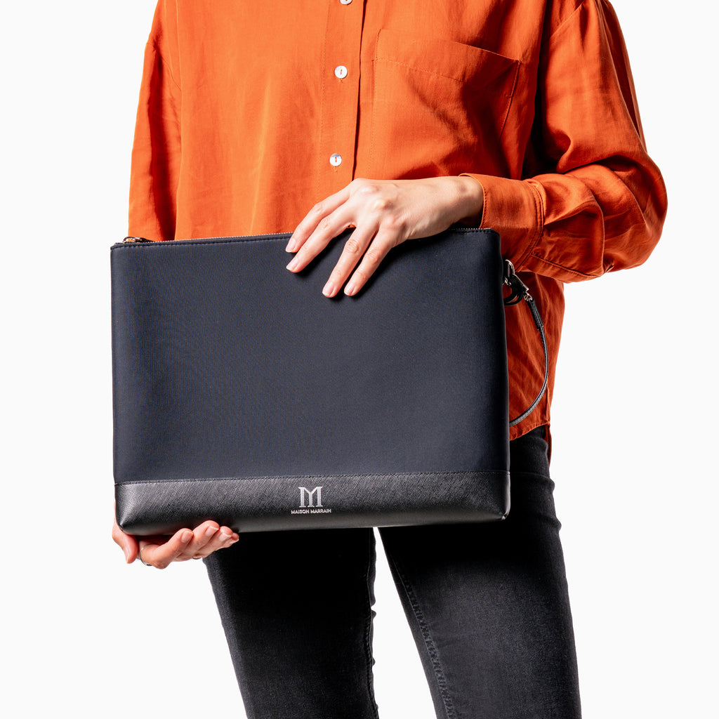 femme tenant une grande pochette noire Maison Marrain deux vie pour ordinateur portable ou documents en néoprène avec bordure en cuir durable noir