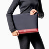 Woman in black holding Maison Marrain deuxvie large black pouch for laptop or documents made from neoprene with durable red bordeaux leather trim