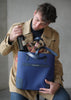 Homme attrapant une bouteille de vin de DeuxMag All Weather big Tote bag bleu en néoprène et cuir