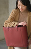 Asian woman with coat holding Maison Marrain DeuxVin leather tote Bag in red bordeaux 