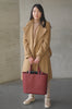 Femme asiatique avec manteau et baskets tenant un sac fourre-tout en cuir Maison Marrain DeuxVin en rouge bordeaux