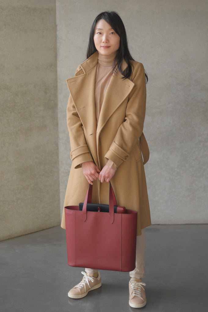 Asian woman with coat and sneakers holding Maison Marrain DeuxVin leather tote Bag in red bordeaux 