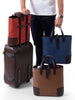 homme avec une valise contenant trois tote bags Deuxmag en bleu rouge et marron