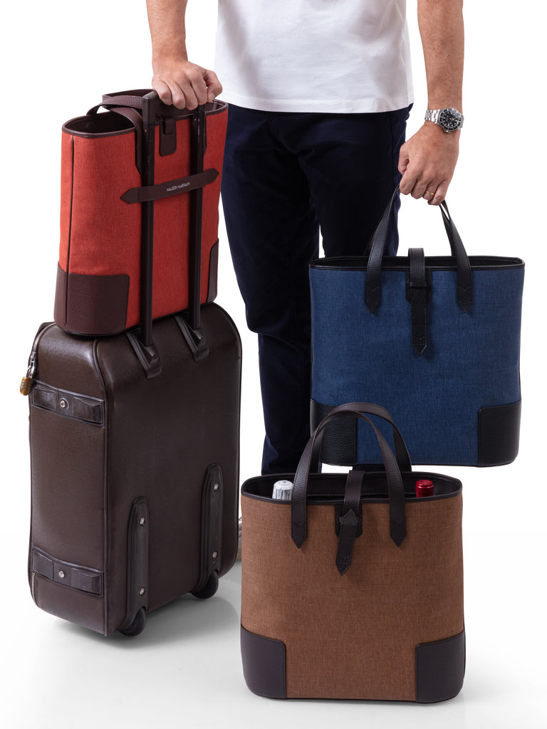 man with a suitcase holding three Deuxmag tote bags in blue red and brown