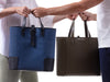 A couple holding the Deuxmag in black and blue and the Deuxvin in green tote bags