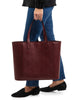 woman walking holding Maison Marrain DeuxVin leather tote Bag in red bordeaux
